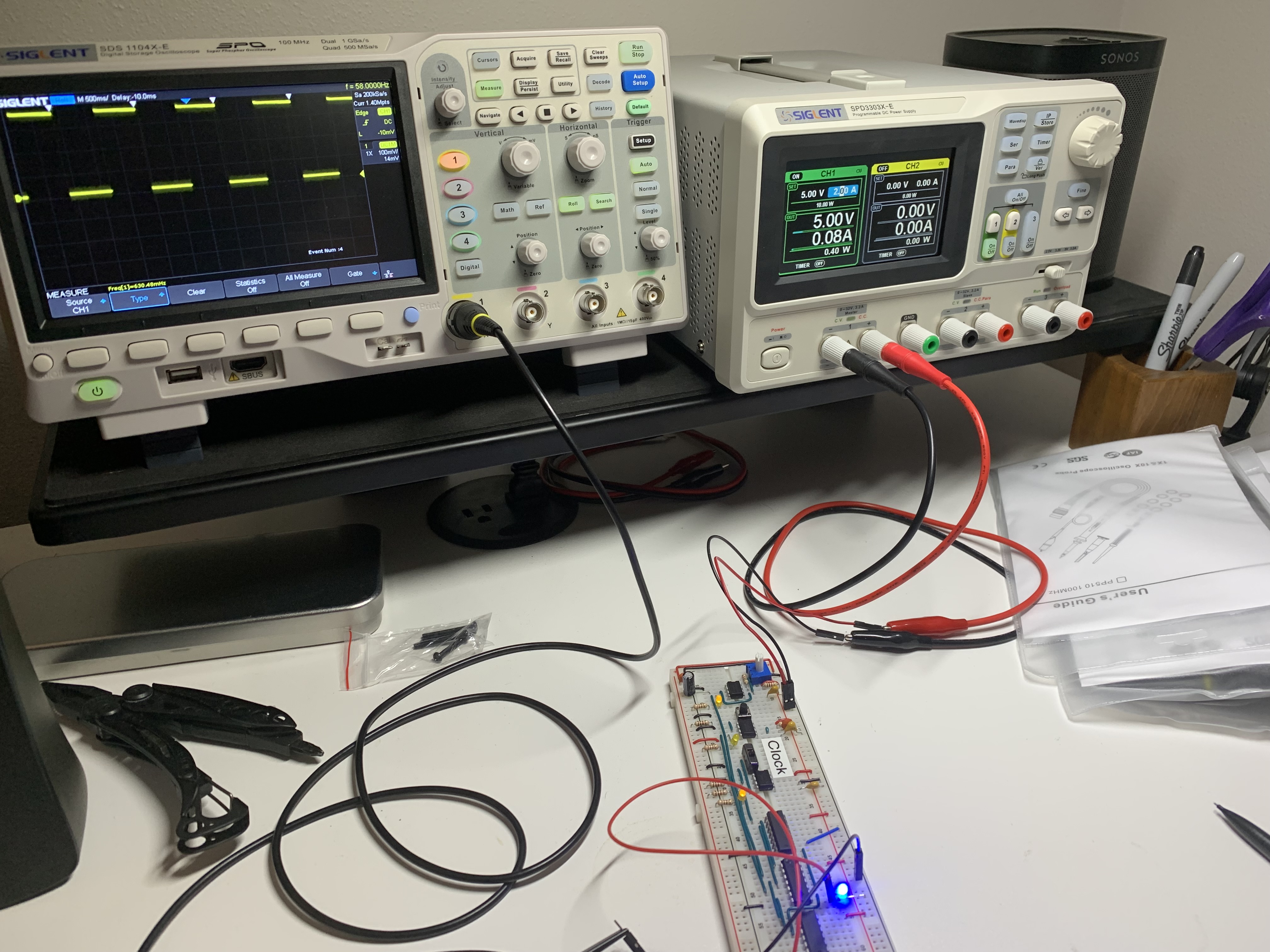 An image of an oscilloscope and bench power supply on a desk connected to a breadboard, showing the clock frequency on the oscilloscope.